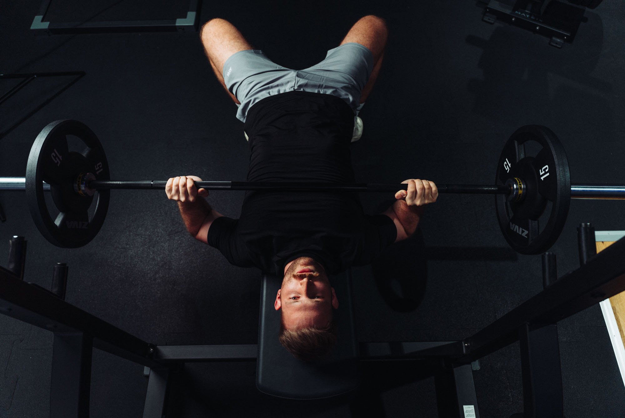 Person trains on a bench press station in the FITOMAT studio with a barbell.